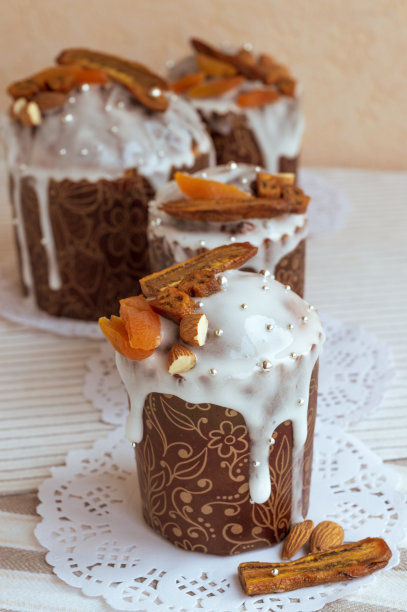 复活节自制的蛋糕放在白色的餐巾上，上面装饰着干香蕉、橙色杏子、杏仁和优雅的小糖银珍珠珠。四个时尚蛋糕的垂直照片图片下载