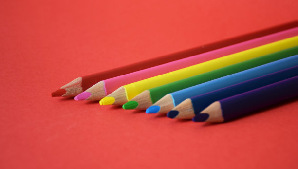 彩虹色的彩色铅笔平躺在红色背景旁边图片下载