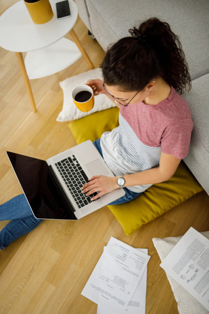 年轻女子坐在家里的地板上用笔记本电脑和文件工作图片下载