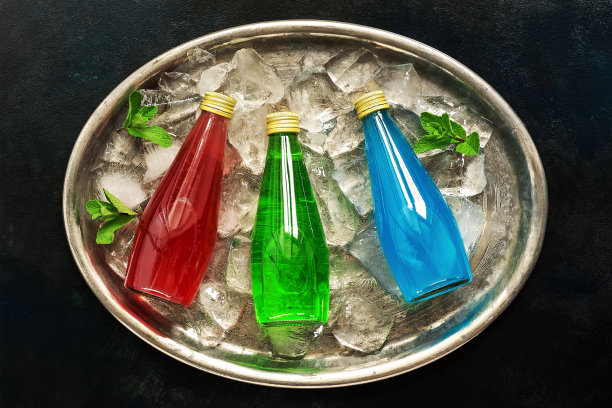 清爽的彩色饮料装在瓶子里，红色，绿色，蓝色的托盘上加冰和薄荷叶。俯视图，平放。图片下载