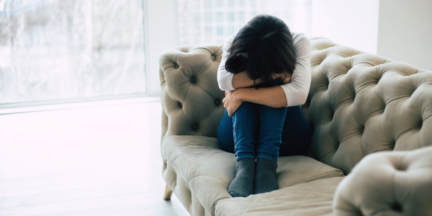 独自挣扎。一个孤独的女人坐在她的沙发上，拥抱她的膝盖和隐藏她的头哭泣的特写照片。图片下载