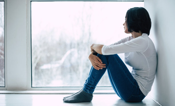 闭关锁国则。摧毁一个悲伤的女人的特写照片，她是抱着她的膝盖，坐在窗台上，看着窗外。图片下载