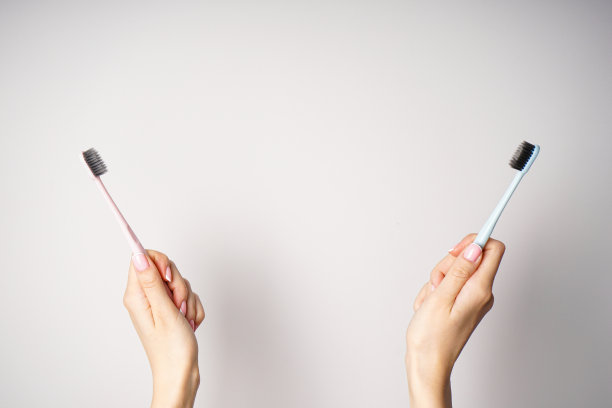一位灰色背景的年轻女子手中拿着黑色刷毛的彩色牙刷。文字空间，俯视图。图片下载