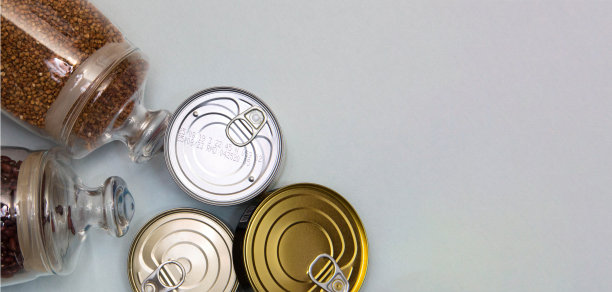 横幅。食物捐赠，蓝色背景。散装产品容器内的豆类、荞麦。黄鸡蛋放在纸板盘里。罐头食品装在罐头里。为文本留出空间。垂直的照片。图片下载