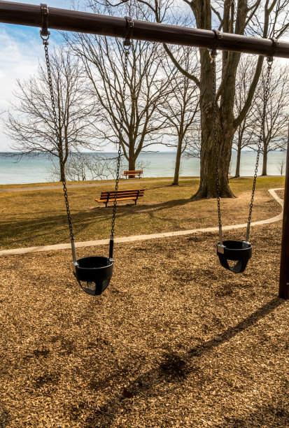 空旷，孤立的秋千在一个孩子的操场上和一个湖的景色。图片下载