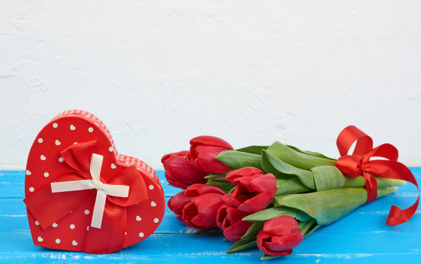 一束红色盛开的郁金香和绿色的叶子，包装礼物在蓝色的木制背景图片下载