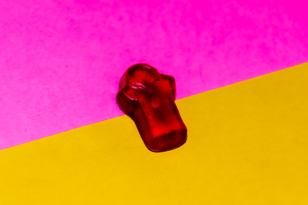 这是一张红色果冻糖的特写照片，它穿着polo衫，打着领带，背景是充满活力的黄色和粉色图片下载