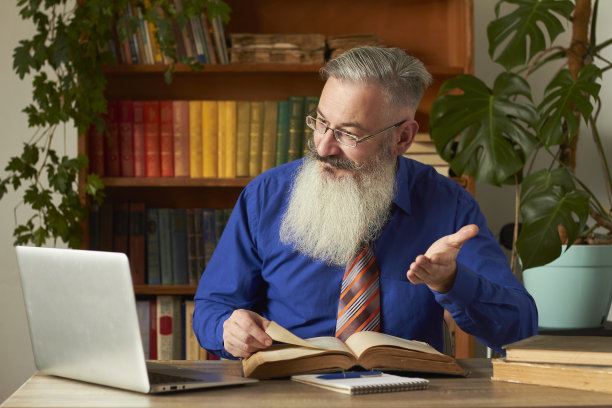 远程学习的概念。教师教授导师在线教授纪律。成熟的大胡子男士通过笔记本电脑回答老师的问题。图片下载