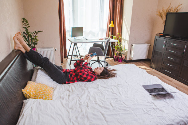 无聊的女人躺在床上玩手机。图片下载