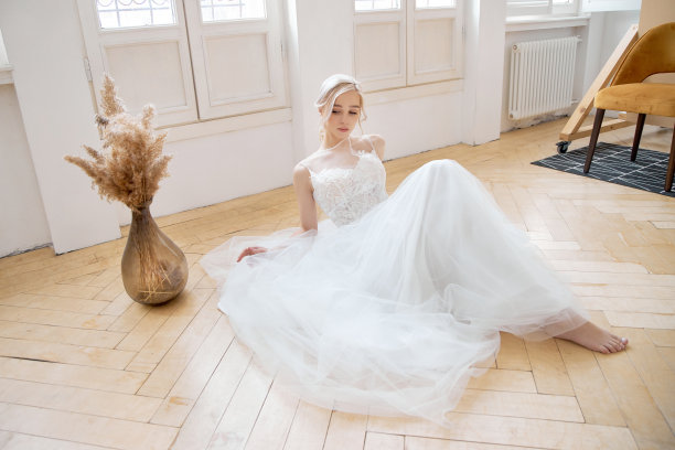 金发女郎穿着漂亮的白色婚纱坐在地板上。新娘在婚礼前等待新郎图片下载