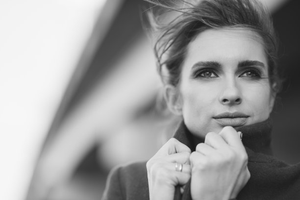 在冰封的桥下，一个穿着大衣围着围巾的美丽孤独的女人用手抓住自己的衣领。孤独的概念。黑白艺术照片。软的焦点。图片下载