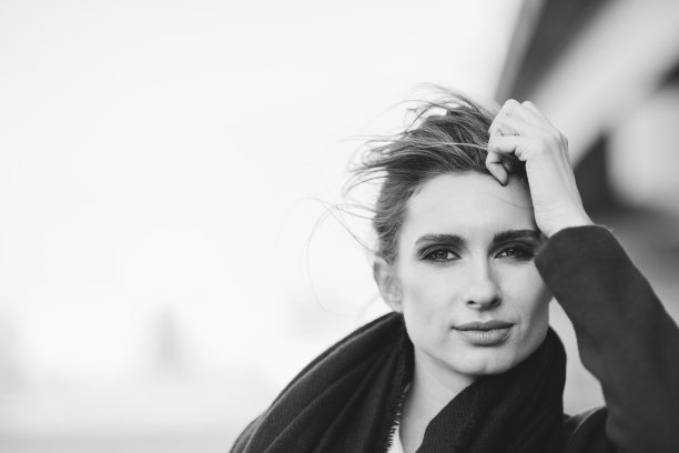 一个美丽孤独的女人，穿着大衣，围着围巾，头发在寒冷灰暗的日子里在桥下随风飘动。孤独的概念。黑白艺术照片。软选择聚焦。图片下载