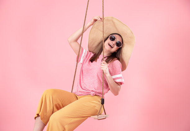 年轻女子在粉红色的背景下荡秋千。图片下载