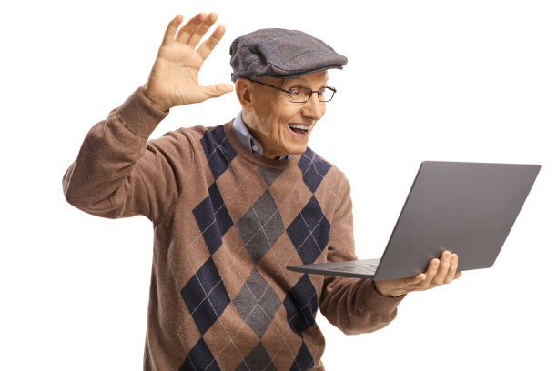一位老人对着一台笔记本电脑的网络摄像头边挥手边说话图片下载