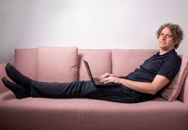 一个神色沮丧的男人在家工作。躺在沙发上。图片下载
