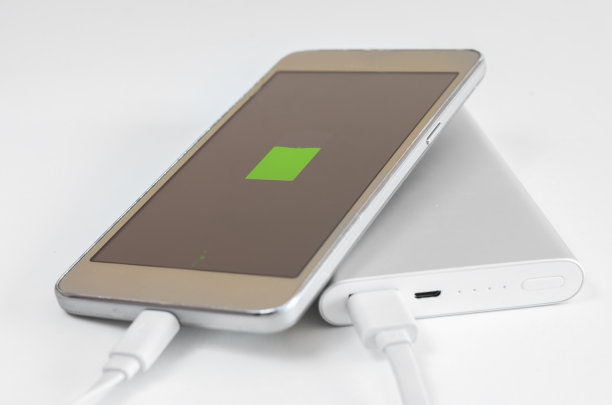 空白的智能手机电池在白色背景上充电的特写。旅行充电装置的外部溶质。图片下载