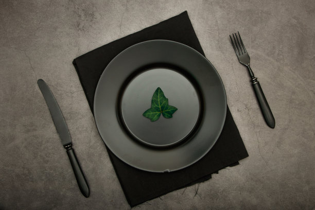 黑色陶瓷盘子和一套餐具。在黑色的背景下，空着黑色的盘子吃早餐、晚餐或喝茶。从以上观点。拷贝空间是你的个人文本。黑色的照片。优雅的黑色餐具。图片下载