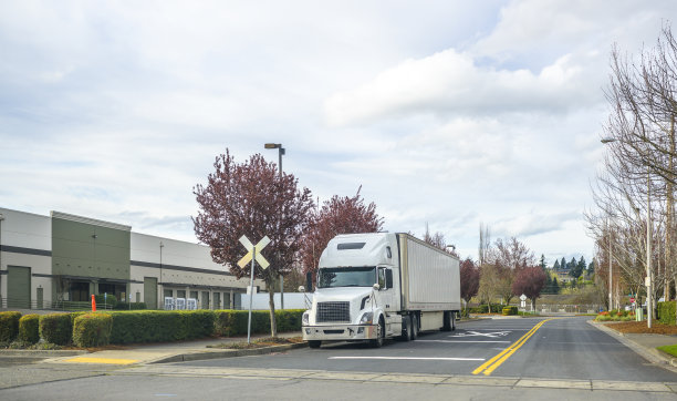 白色大卡车和冰箱半挂车站在靠近仓库停车场的道路上图片下载