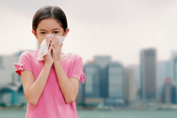 亚洲可爱女孩对空气污染或病毒、COVID - 19有过敏症状和流鼻涕。一个孩子用纸巾保护她的鼻子还模仿了太空城市的背景。图片下载