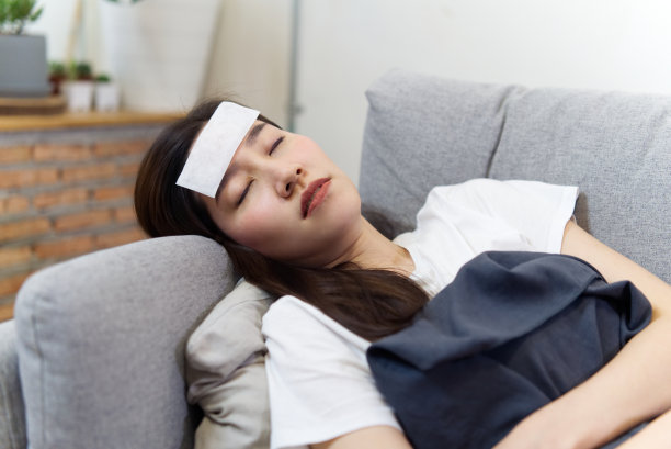 不健康的亚洲漂亮女孩发烧闭着眼睛睡在家里的沙发上。她在额头上敷了一块退烧贴片，并用毯子盖住自己。疾病和疾病的概念。图片下载