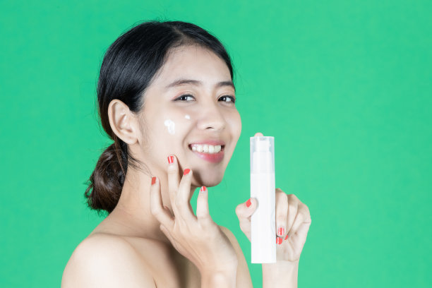 美丽健康的年轻亚洲女人拿着容器与面霜在绿色孤立的背景。化妆品和护肤品的概念。图片下载