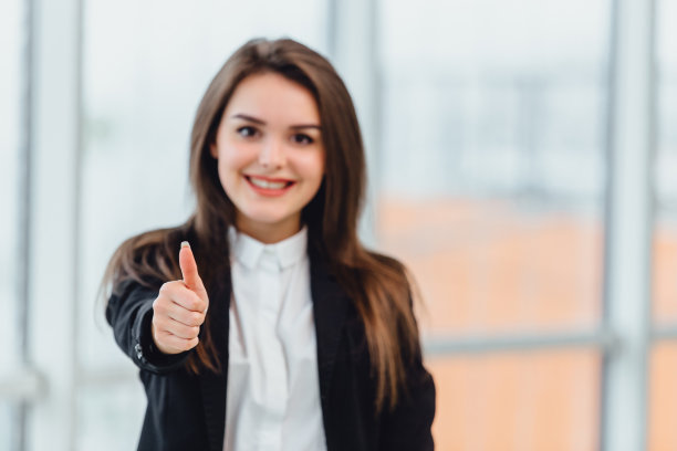 特写的漂亮的办公室雇员显示拇指向上孤立近窗户。关注最前面的手势。图片下载