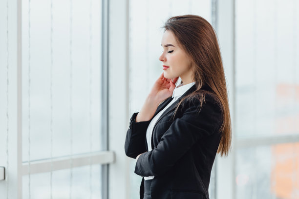 在她的新办公室里，一个快乐的女人站在窗前，表现出愉悦的情绪和自信。图片下载