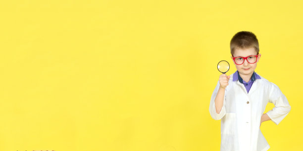 戴着眼镜，穿着病号服，戴着放大镜，背景是黄色。小科学家做发现，做实验。寻找治愈方法，病毒疫苗。未来的概念。横幅图片下载
