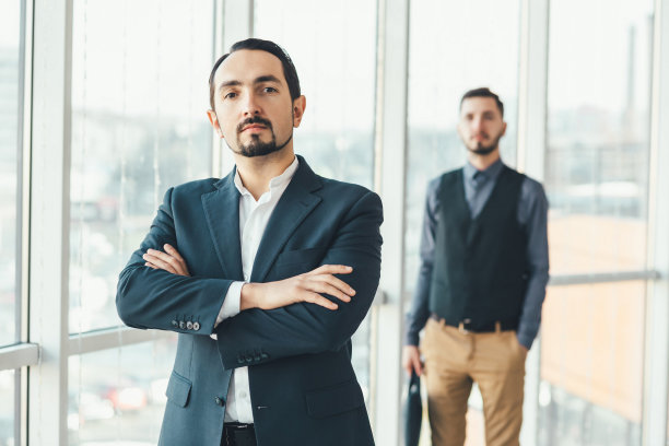 自信的商人站在最前面，双手交叉，看着镜头，而他被击败的竞争对手站在后面。图片下载