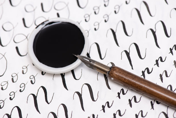 木制背景上的书法纸、笔尖、纸、墨。英文字母是用画笔写的。图片下载