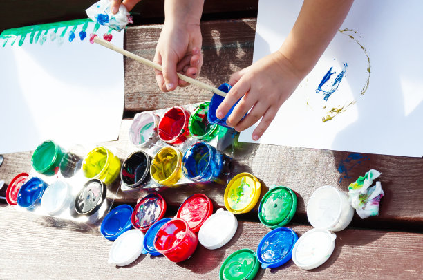 孩子的手在白色的背景上画水粉颜料。打开装有多种颜色颜料的罐子。用画笔蘸颜料。在户外。孩子的爱好和活动。图片下载