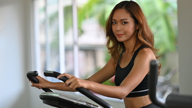 照片美丽的运动女人在黑色背心运动套装做“运动与健身机器在现代健身馆为背景。健身的女孩的概念。图片下载