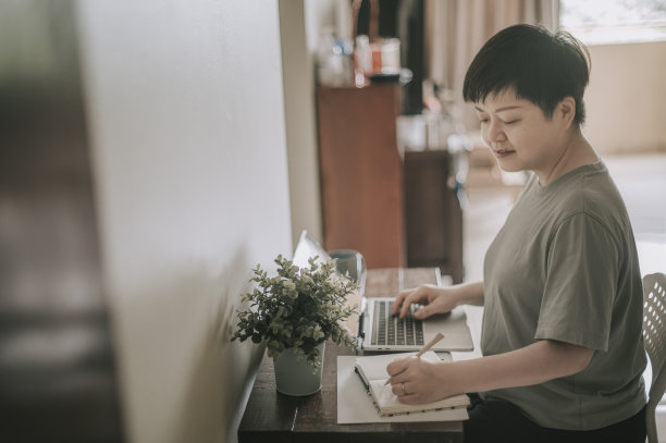 一位中年亚裔华人女性在家里用笔记本电脑写笔记图片下载