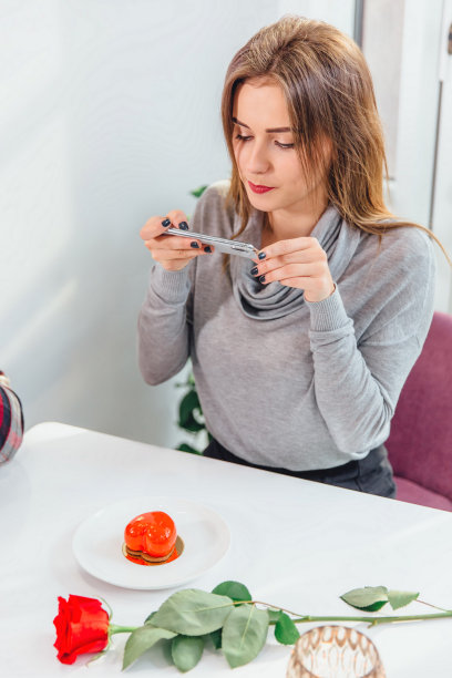 社交媒体营销概念。可爱的年轻女士拍照的一个甜甜点在咖啡馆，使flatlay和看起来参与她的工作。图片下载