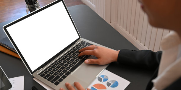 这张照片是一个商人坐在黑色的办公桌前用笔记本电脑打字的照片，背景是井然有序的办公室。图片下载