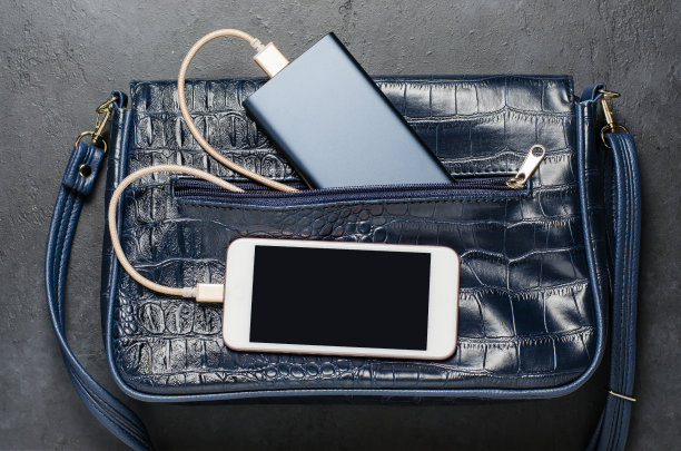 蓝色电源银行和女士包里的智能手机。深灰色的混凝土背景。图片下载