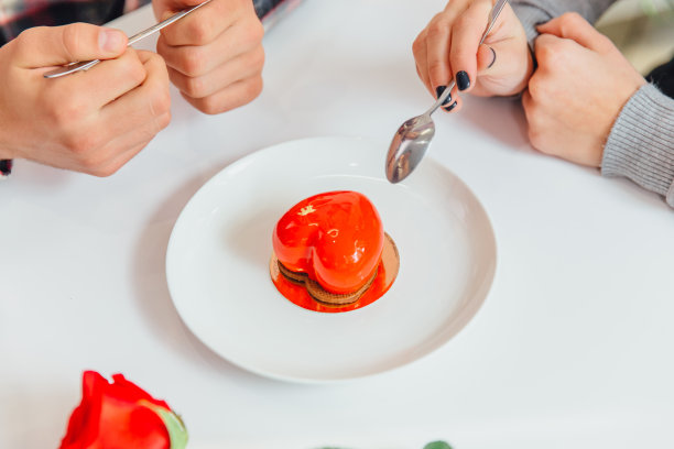 心形的慕斯甜点和人们手牵手，握着勺子，品尝着这种糖果，庆祝情人节。图片下载