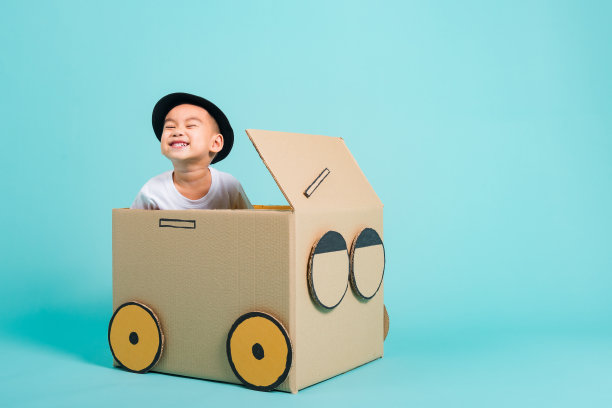 快乐亚洲儿童男孩微笑在驾驶玩车创意由纸板箱想象，暑假旅游概念，工作室拍摄的蓝色背景与文本复制空间图片下载