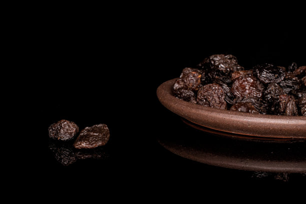 隔在黑色玻璃上的干黑葡萄干图片下载