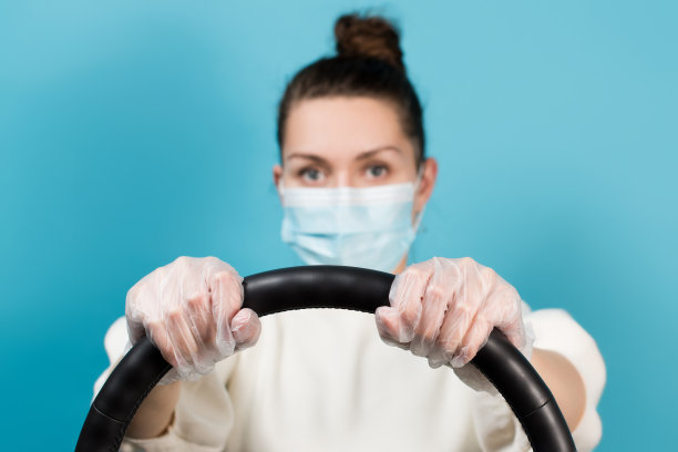 戴着医用口罩的女孩紧握方向盘，双手戴着手套。图片下载