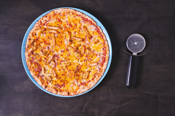 俯视图，一个新做的比萨饼盘在一个黑色的木制桌子上，旁边有一个比萨饼切割机图片下载