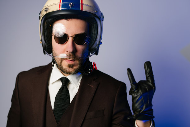 摩托车手穿着西装，戴着头盔，做着摇滚喇叭手势图片下载