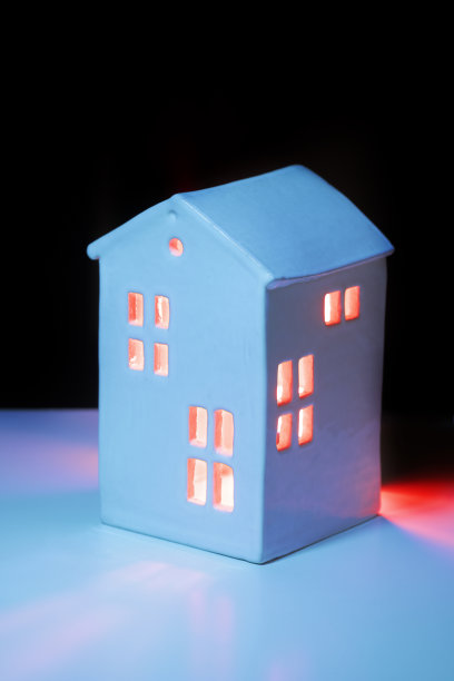 一个小小的玩具舒适的陶瓷房子在夜晚从窗户里透出来的光。晚上待在家里的概念。垂直拍摄与路径黑色部分的顶部文字图片下载