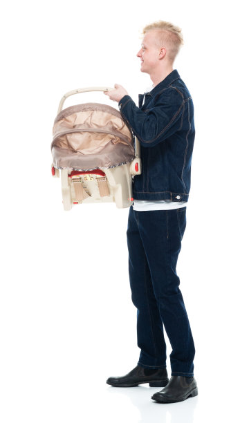 白人婴儿-人类年龄站在白色背景穿着t恤和持有汽车安全座椅图片下载