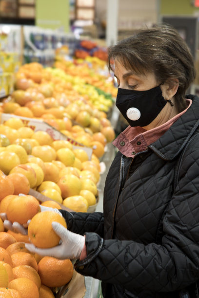 戴着口罩和手术手套的妇女在超市比较橙子图片下载