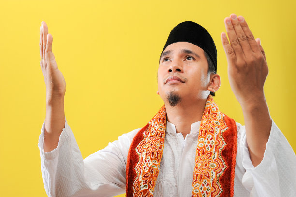 一个年轻的亚洲穆斯林男子祈祷举起他的手穿着穆斯林服装，低角度和特写图片下载
