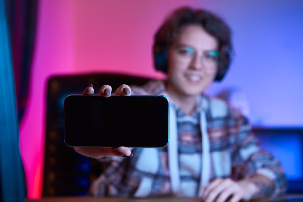 年轻漂亮的女人戴着眼镜和无线耳机在摄像头前显示智能手机的屏幕图片下载