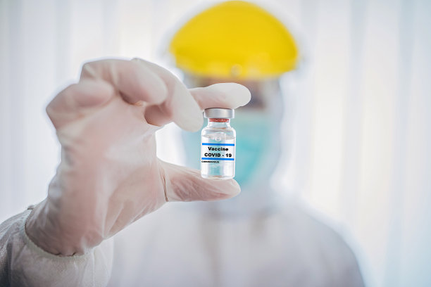 身穿防护服的医生，手持装有Covid-19冠状病毒疫苗的试管素材图片