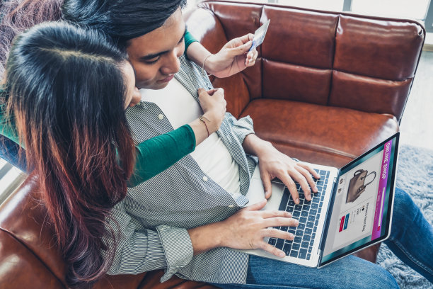 年轻夫妇在家里用信用卡在网上购物。信用卡上的号码是伪造的。信用卡上没有显示个人信息。网上商业购物概念。图片下载