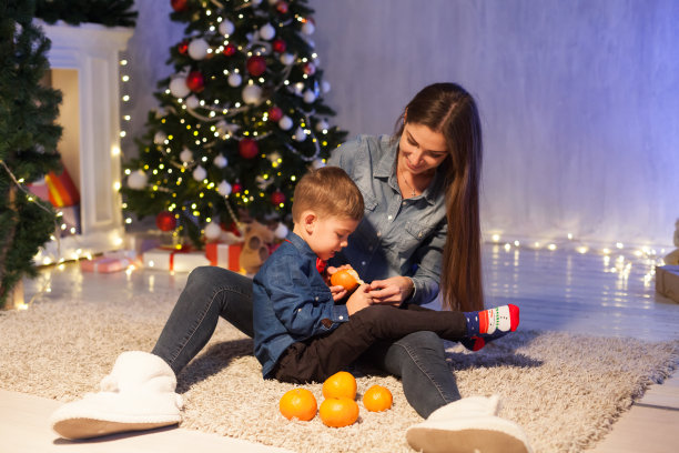 妈妈和儿子在新年前夕在圣诞树上点亮礼物花环图片下载